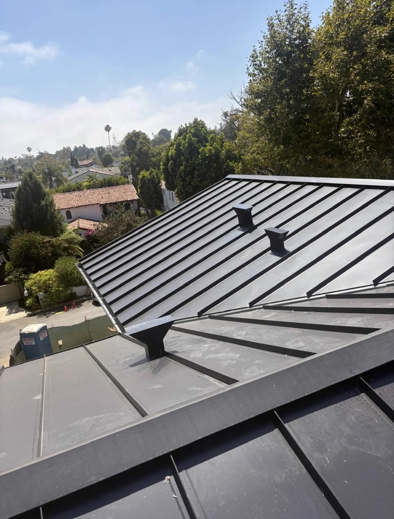 Standing seam metal roof ridge with black roof vents and factory-finished panels