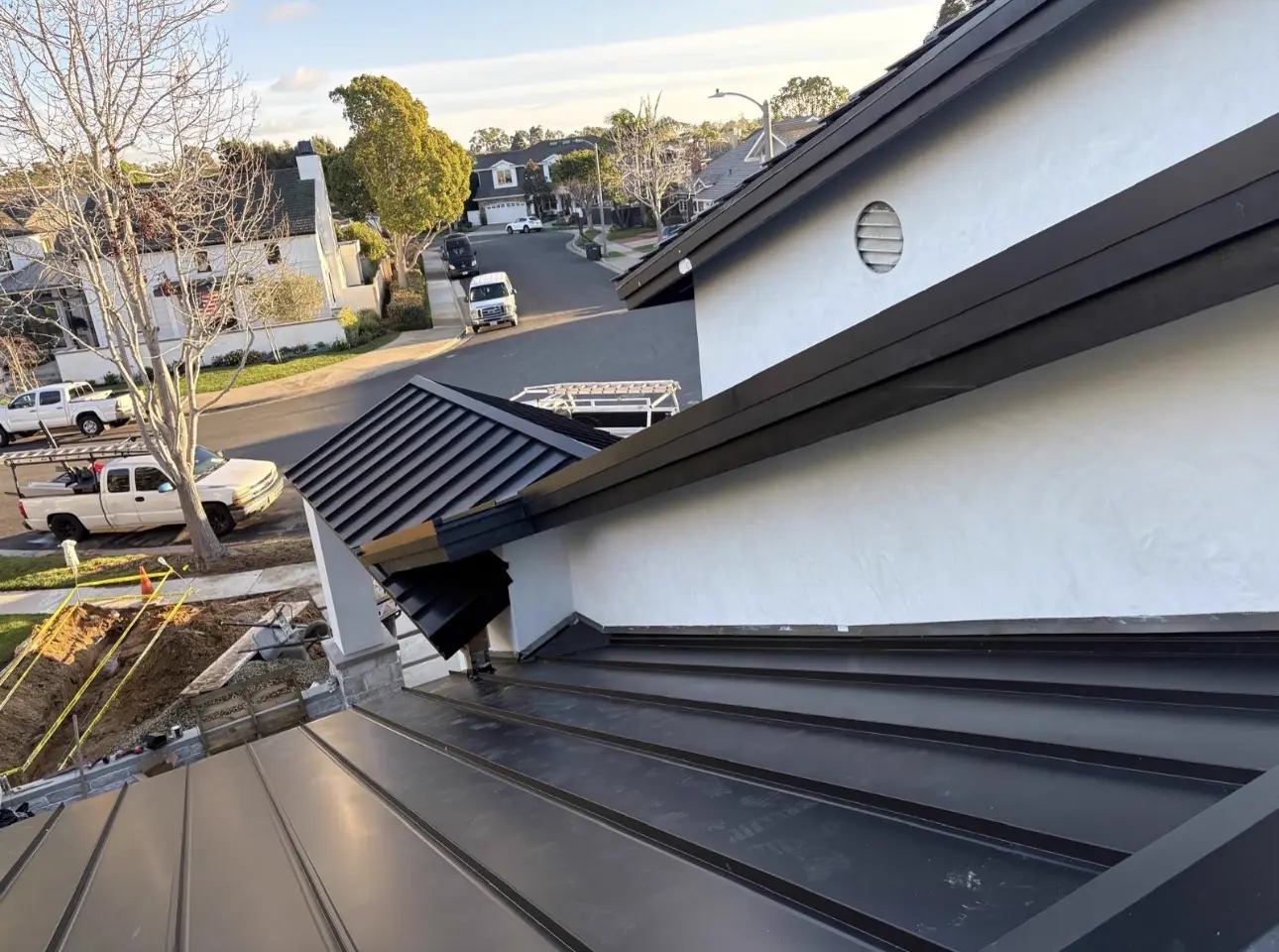 Dark standing seam metal roof with dormer and stucco sidewall flashing on a residential street