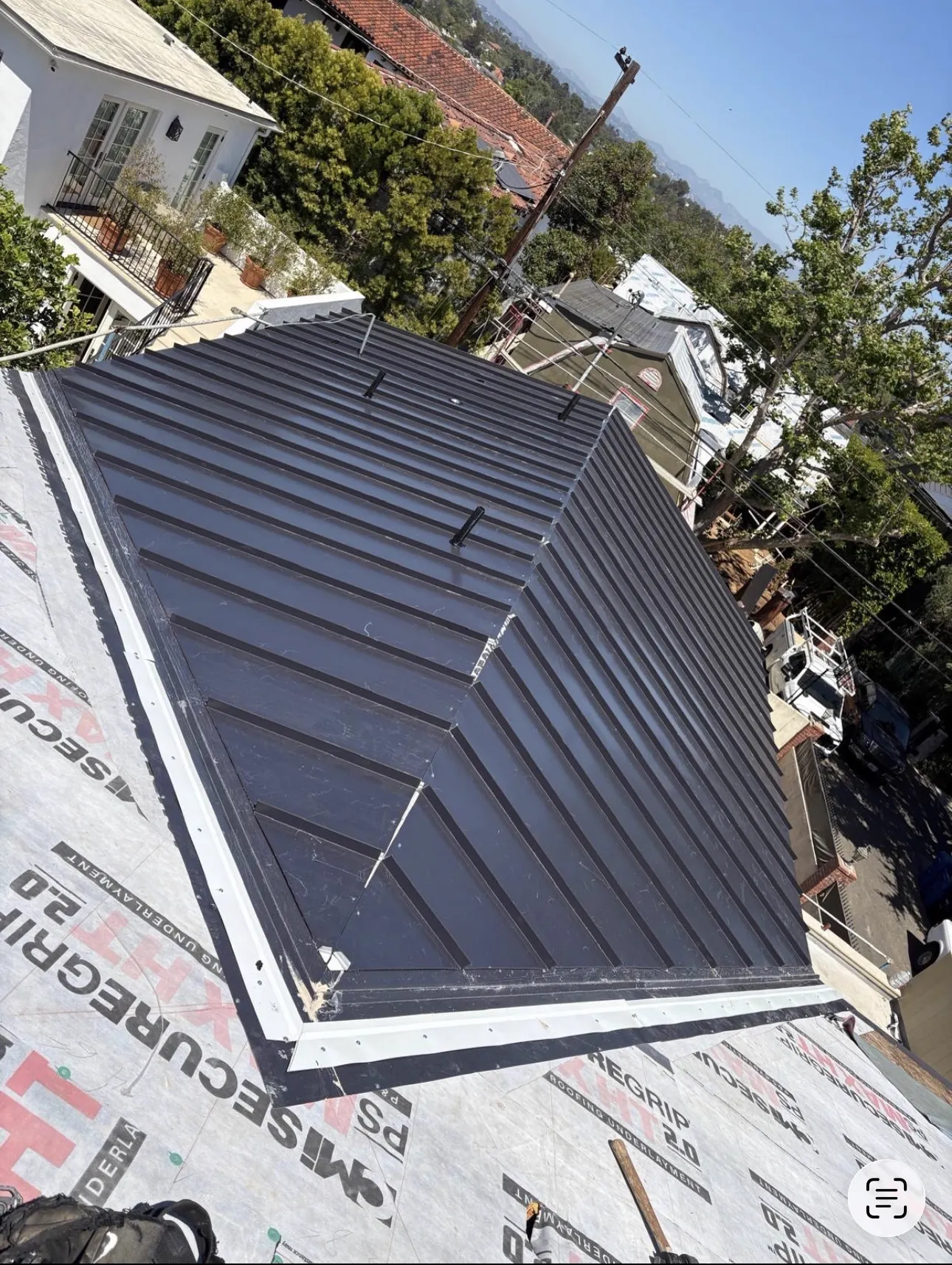 Aerial view of a dark standing seam metal hip roof over peel-and-stick high-temperature underlayment