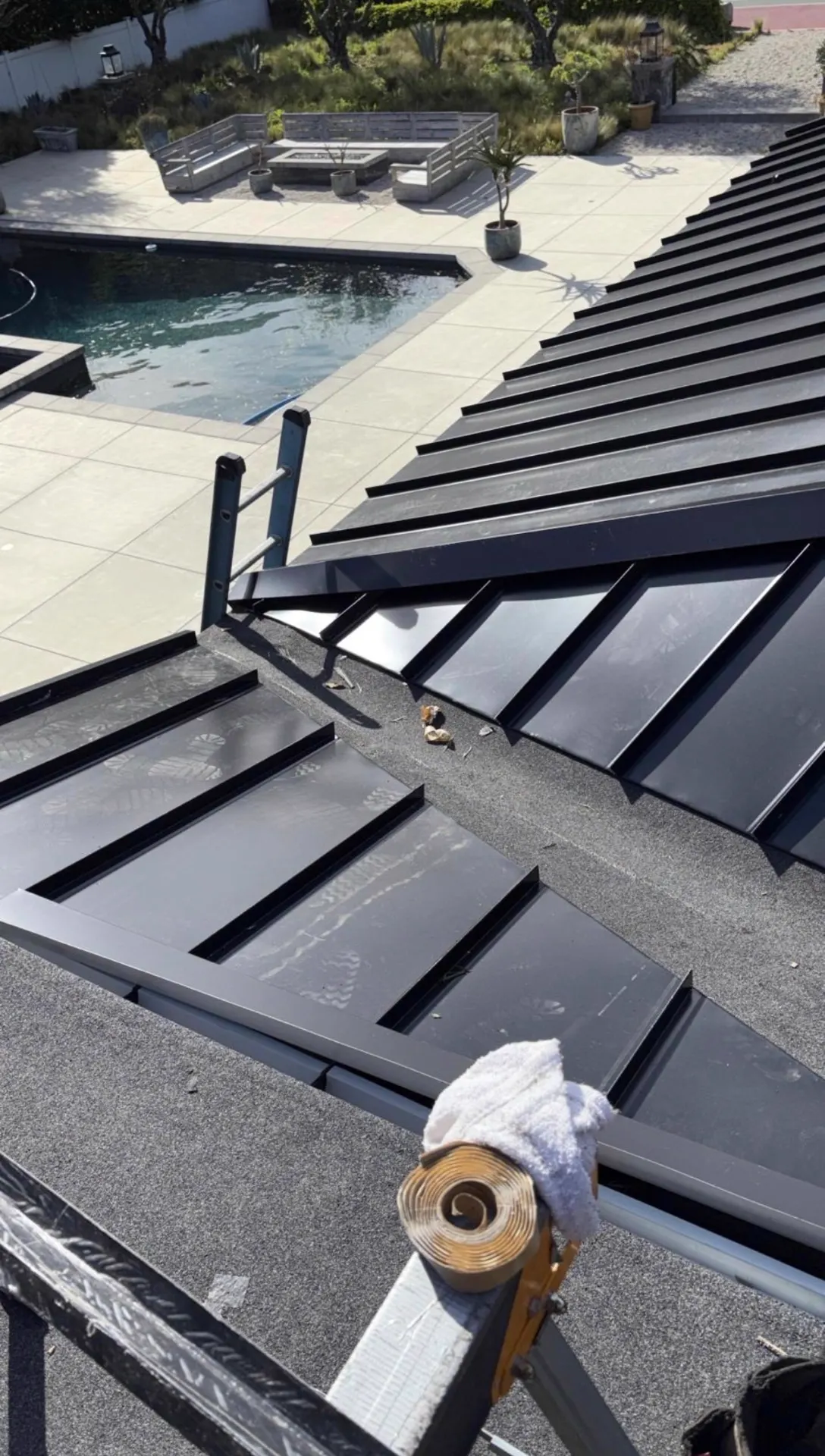 Standing seam metal roof panels and valley detail above a backyard pool deck