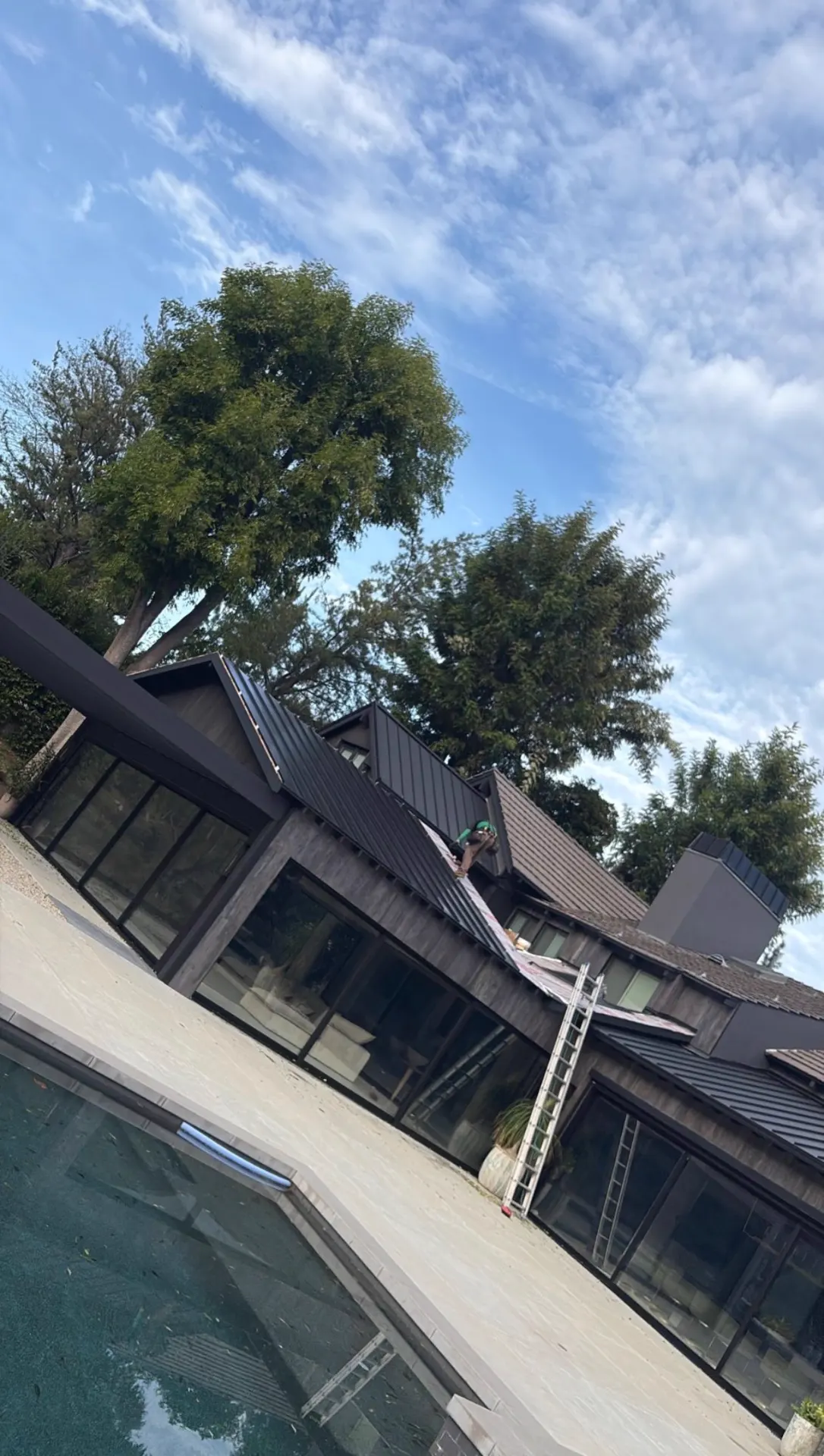 Roofing crew installing standing seam metal panels on a mid-century home beside a swimming pool